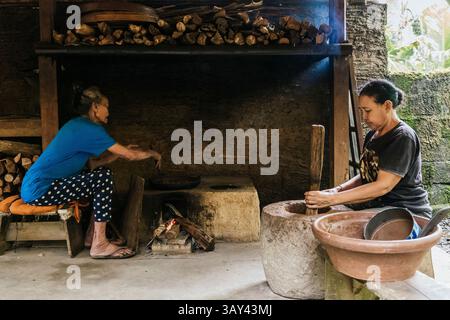 Zwei Frauen kochen in einer rustikalen Küche. Der eine benutzt einen Steinmörtel für Kaffee, der andere für einen Holzofen Stockfoto