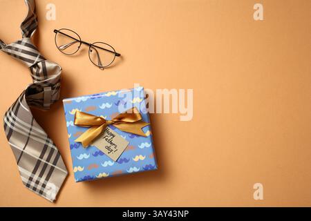 Draufsicht eines Vatertagsgeschenkes, das in einer dekorativen Box mit Schleife gewickelt ist, zusammen mit einer stilvollen Krawatte und einer Brille, die alle in einem einfarbigen Orange gehalten sind Stockfoto