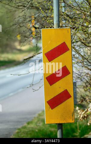 Ein gelbes Warnschild mit drei roten Linien warnt die Fahrer vor einer bevorstehenden Eisenbahn, die im Frühjahr von Grün umgeben ist Stockfoto