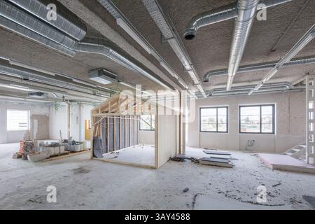 Innenraum eines modernen Bürobereichs im Bau, mit freiliegenden Kanälen, unfertigen Wänden und großen Fenstern. Betont das industrielle Design A Stockfoto