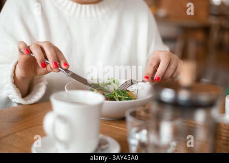Nahaufnahme einer Frau, die ein Frühstücksgericht in gemütlicher Atmosphäre in einem Café genießt. Die Tischeinstellung umfasst eine Schüssel mit Pilzkoteletts mit Kartoffeln und Stockfoto