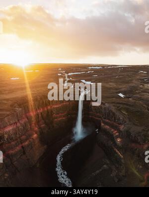 Sonnenuntergang aus der Vogelperspektive des Hengifoss-Wasserfalls in Ost-Island mit dramatischen Basaltklippen mit roten Schichten und Wasserkaskaden in einen tiefen Canyon. Stockfoto