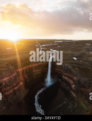 Luftaufnahme des Hengifoss-Wasserfalls bei Sonnenuntergang mit leuchtenden roten Felsschichten und dramatischen Klippen in Islands abgelegenem östlichen Hochland. Stockfoto