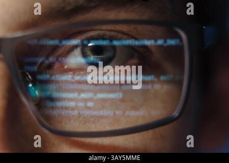 Extreme Nahaufnahme eines Programmierers oder Softwareentwicklers mit Computercode, der auf einer Brille reflektiert wird und die Cybersicherheit, Programmierung und Entwicklung künstlicher Intelligenz symbolisiert. Data Science-Konzept Stockfoto
