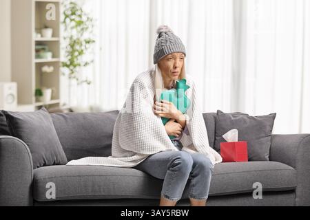 Frau, in Decke gewickelt, auf einem Sofa sitzend und mit einem Körperwärmer in der Hand Stockfoto