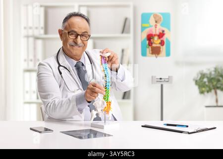 Reifer männlicher Arzt untersucht ein Modell der Halswirbelsäule in der Praxis Stockfoto
