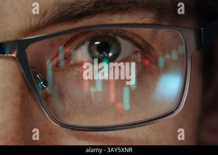 Nahaufnahme eines Kryptohändlers oder Investors Auge mit Kerzendiagrammen und Finanzgrafiken, die sich in seiner Brille widerspiegeln. Kryptowährung oder Börsenkonzept Stockfoto