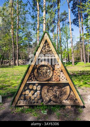 Großes Holzinsektenhotel (Insektenhaus) in sonniger Waldparklage. Dreieckiger A-Rahmen-Schutz für Insekten. Umweltfreundliches Insektenhotel voller Natur Stockfoto