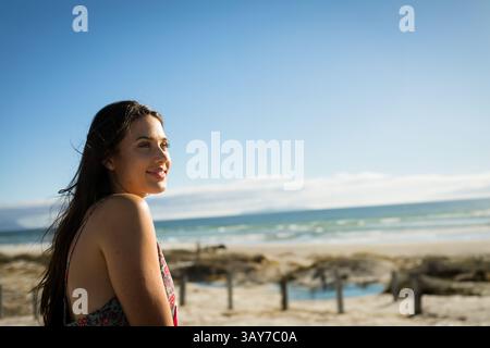 Junge Frau, die an verwitterten Pfosten und Seilzäunen am Strand steht, auf das Meer blickt, Kopierraum Stockfoto