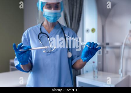 Pfleger mit Maske und Gesichtsschutz bei der Handhabung von Nasopharynxtupfern im klinischen Versuchsraum Stockfoto