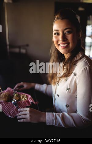 Junge Frau isst Burger und Pommes im karierten Korb am Tisch im gemütlichen Café, Kopierraum Stockfoto