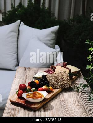Kunstvoll gestaltete Wurstplatte mit verschiedenen Käsesorten, frischem Obst, Brot und Marmelade, präsentiert auf einem rustikalen Holztisch. Stockfoto