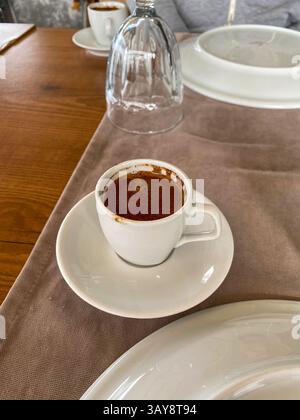 Eine Tasse frisch gebrühten türkischen Kaffee, serviert auf einer weißen Untertasse auf einem Holztisch mit neutraler Einrichtung. Stockfoto