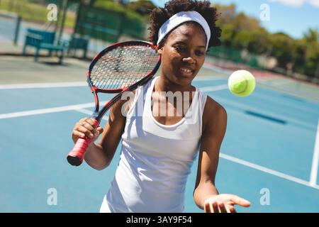 Tennisspielerin mit Tennisschläger, die Tennisball mit Kopfband auf den Platz im Freien wirft Stockfoto