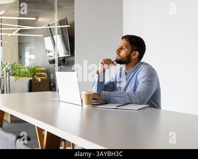 Mann sitzt am Tisch im Großraumbüro, mit Laptop, Kaffeetasse und Notizbuch, Kopierraum Stockfoto