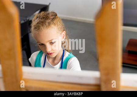 Weibliche Kindermalerei auf Leinwand hinter hölzerner Staffelei im Kunststudio mit schwarzem Tisch Stockfoto