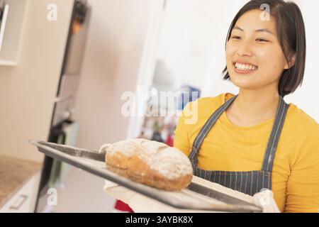 Asiatische Frau, die frisch gebackenen Brotlaib auf Blech in der Küche hält, Kopierraum Stockfoto