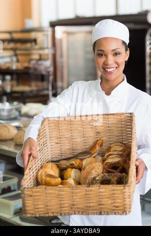 Afroamerikanischer Bäcker, der in der Bäckerei steht und einen Korb mit Brot und Gebäck hält, lächelnd Stockfoto