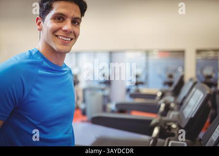 Mann, der in einer Reihe von Laufbändern und Ellipsentrainer im hellen Fitnessstudio steht, in die Kamera lächelt, Kopierraum Stockfoto