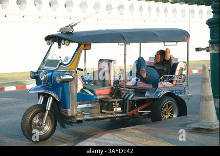 Ein Tuk-Tuk-Fahrer sitzt bequem in seinem geparkten Fahrzeug Stockfoto