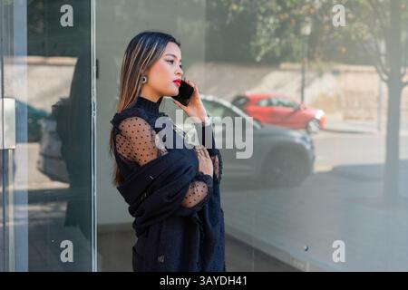 Eine stilvolle und modische Frau führt draußen in einer pulsierenden städtischen Umgebung ein Telefongespräch Stockfoto
