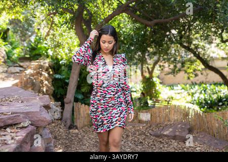 Eine junge Frau geht anmutig durch einen üppigen und farbenfrohen Garten, während sie ein lebendiges und elegantes Kleid trägt Stockfoto