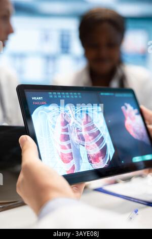 Mediziner und seine Mitarbeiter treffen sich, um die Lungenradiographie für die Patientenversorgungsstrategie in einem Behandlungszentrum zu diskutieren. Das medizinische Team analysiert Röntgenaufnahmen und Krankenakten von Organen, um sich auf die Diagnostik zu konzentrieren. Nahaufnahme. Stockfoto