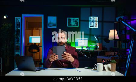 Ein technischer Experte präsentiert ein Tablet im Einstiegssegment mit niedrigen Budgets für interessierte Zuschauer und filmt im Studio. Viraler Content Creator, der digitale Geräte vor dem Internet-Publikum überprüft, Kamera B Stockfoto