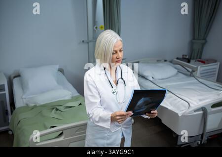 Ärztin, die Röntgenfilm im Krankenhauspatientenzimmer untersucht, mit zwei Betten und Stethoskop Stockfoto