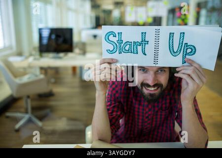 Ein Mann mit mittlerem Erwachsener hebt das spiralförmige Notizbuch über den Kopf in einem modernen Büro mit farbenfrohen Haftnotizen Stockfoto