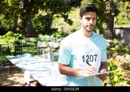 Mittelgroßer Mann mit Race Lätzchen 1207, stehend am Klapptisch in grünem Park, der auf dem Klemmbrett steht Stockfoto