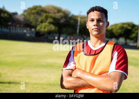 Männlicher Athlet, der auf dem grasbewachsenen Sportplatz steht, trägt ein orangefarbenes Lätzchen mit rot-weißem Jersey, Kopierraum Stockfoto