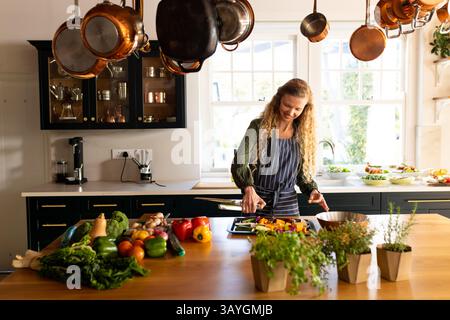 Frau hackt Gemüse auf Holzinsel in der Bauernküche, mit Topfkräutern und Kupfertöpfen Stockfoto