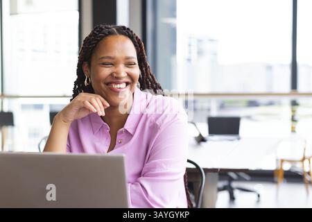 Frau, die am Schreibtisch in einem modernen Büro sitzt und an einem silbernen Laptop mit Blick auf die Stadt arbeitet, Kopierraum Stockfoto