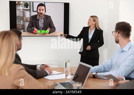 Redner, der über Online-Videochat an der Vorlesung teilnimmt. Publikum und Trainer im Konferenzraum mit Fernseher Stockfoto