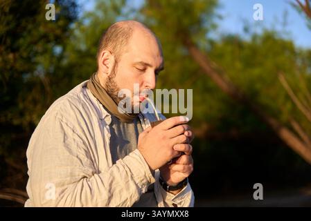 Hispanischer Reisender, der bei Sonnenaufgang am Ufer eines Baches sitzt und die ersten Sonnenstrahlen empfängt, während er Mate trinkt, ein typisches argentinisches Getränk. El Stockfoto