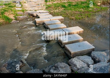 Eine ruhige natürliche Szene mit einem flachen Bach, der sanft durch den Wald fließt, mit Steinsteinen, die das Wasser überqueren. Stockfoto