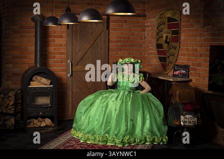 Frau in grünem Kleid sitzt in einem rustikalen Raum mit Kamin und Holzvertäfelung, inszeniertes Fotoshooting, Mindelheim, Unterallgaeu, Bayern, Deutschland, Europ Stockfoto