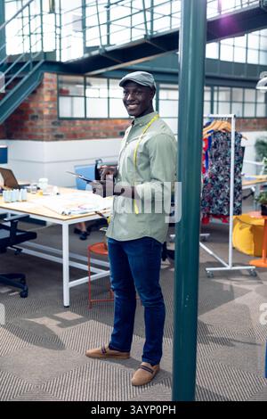 Afroamerikanischer Mann, der Designs auf einem digitalen Tablet mit Bandmaß im Mode-Arbeitsbereich überprüft Stockfoto