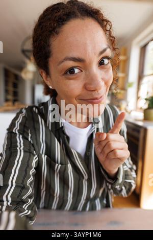 Frau in ihren 30ern, die mit dem Zeigefinger in Richtung Kamera zeigt, in moderner Küche mit natürlichem Licht Stockfoto