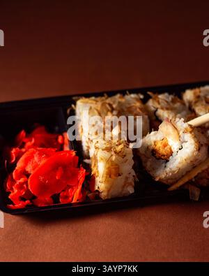 Essstäbchen nehmen eine Portion Sushi-Rolle. Sushi-Brötchen mit Lachs-Frischkäse und Gurke zum Mitnehmen. Konzept für die Lieferung von Lebensmitteln. Stockfoto