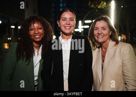 Drei selbstbewusste Geschäftsfrauen lächeln in eleganten Anzügen zusammen und stehen für Empowerment und Teamwork in einem professionellen Ambiente bei Nacht Stockfoto