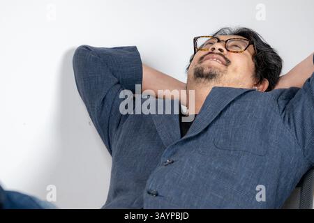 Ein junger Geschäftsmann lehnte sich zurück in seinen Bürostuhl und machte eine kurze Pause von der Arbeit Stockfoto