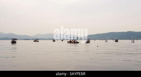 Traditionelle Holzboote mit Touristen, die friedlich auf dem Westsee segeln, umgeben von nebeligen Bergen in Hangzhou, China Stockfoto