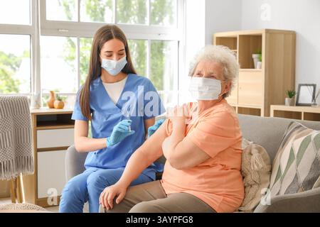 Junge Krankenschwester geimpft Seniorin auf Sofa zu Hause Stockfoto
