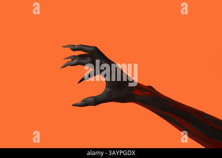 Schwarze Hexenhand mit Klauen auf orangem Hintergrund. Halloween-Feier Stockfoto