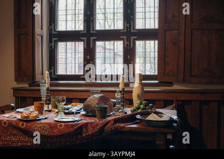 Ein charmanter Esstisch mit Kerzen, frischem Obst und Vintage-Elementen, wunderschön beleuchtet durch ein großes Fenster Stockfoto