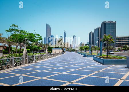 Schöner Fußweg im städtischen Stadtpark mit grünen Bäumen. Blick auf die Corniche Promenade in Abu Dhabi, VAE. Corniche Boulevard Beach Park entlang der Küste Stockfoto