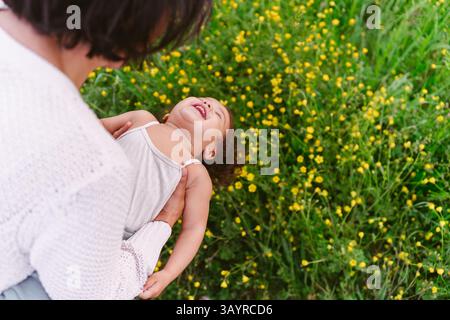Junge tausendjährige Mutter und kleine Tochter, die an einem sonnigen Tag draußen auf Wiesen mit Blumen spielen. Konzept der Mutter-Tochter-Bindung, Kleinkind Stockfoto