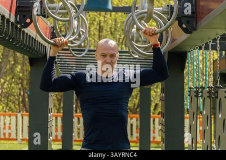 Muskulöser Mann, der Pull-ups und Gymnastikringübungen auf dem Sportplatz macht. Sommer. Öffentlicher Park für Outdoor-Sportarten. Gesunder Lebensstil. Nahaufnahme. Stockfoto